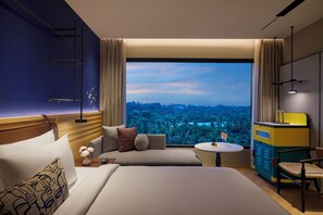 Habitación de hotel con un ventanal grande, una cama, un sofá, una mesita y un minibar.