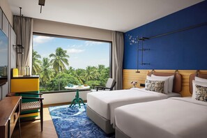 Habitación de hotel con cama, escritorio, silla, una mesita y vistas a palmeras.