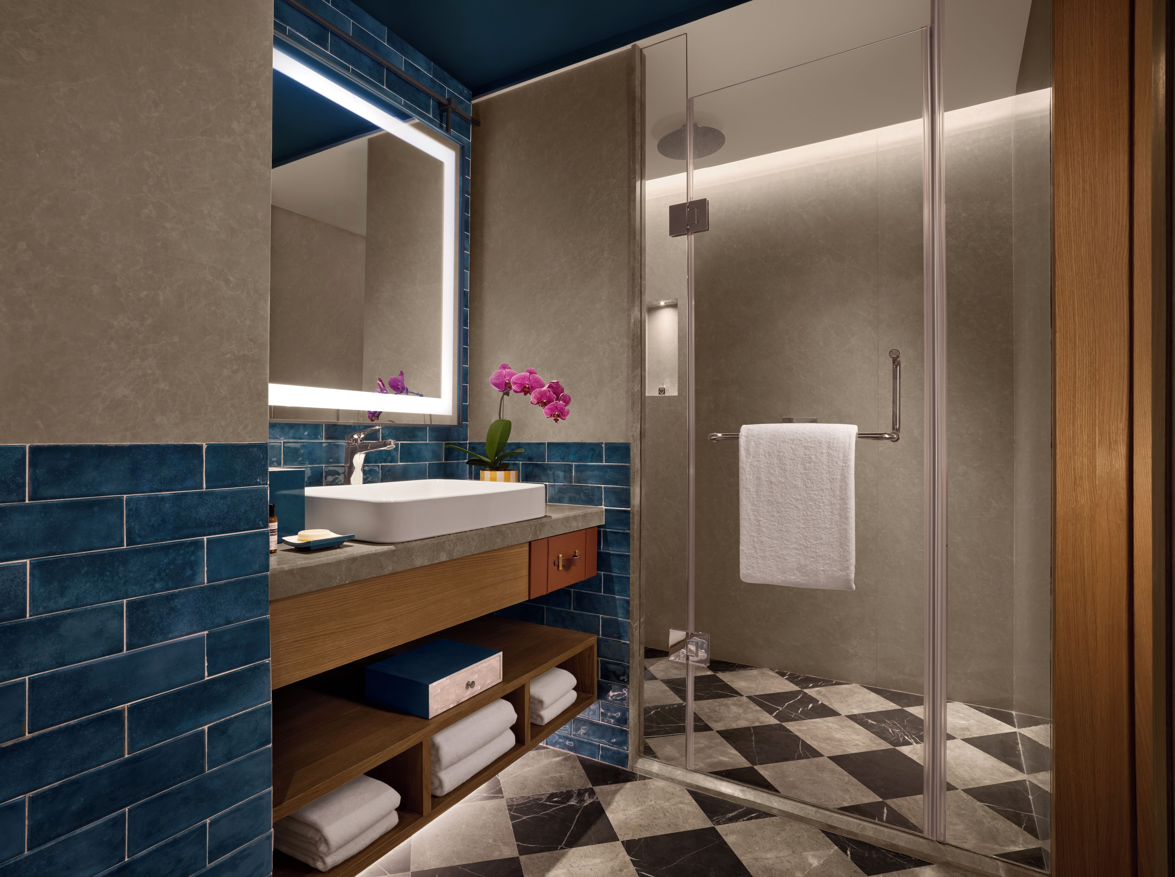 Un baño moderno con ducha de vidrio, lavamanos blanco y salpicadero con azulejos azules.