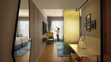 Une chambre d’hôtel avec un grand miroir, un canapé, une petite table avec un vase et un lit recouvert d’un tapis à motifs bleus et blancs.