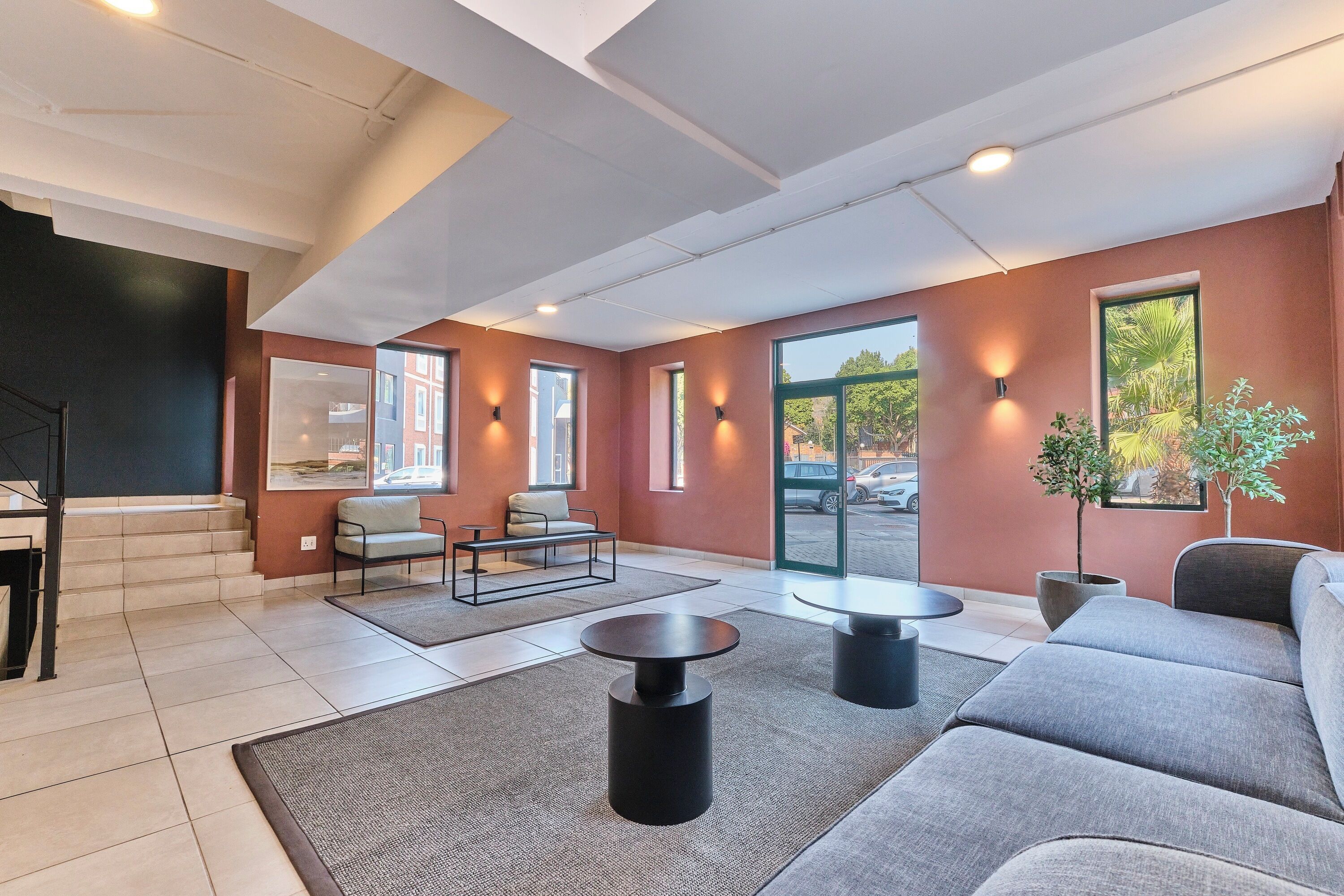 A modern interior with a grey sofa, a coffee table, and a dining table. There are two windows with views of the outside.