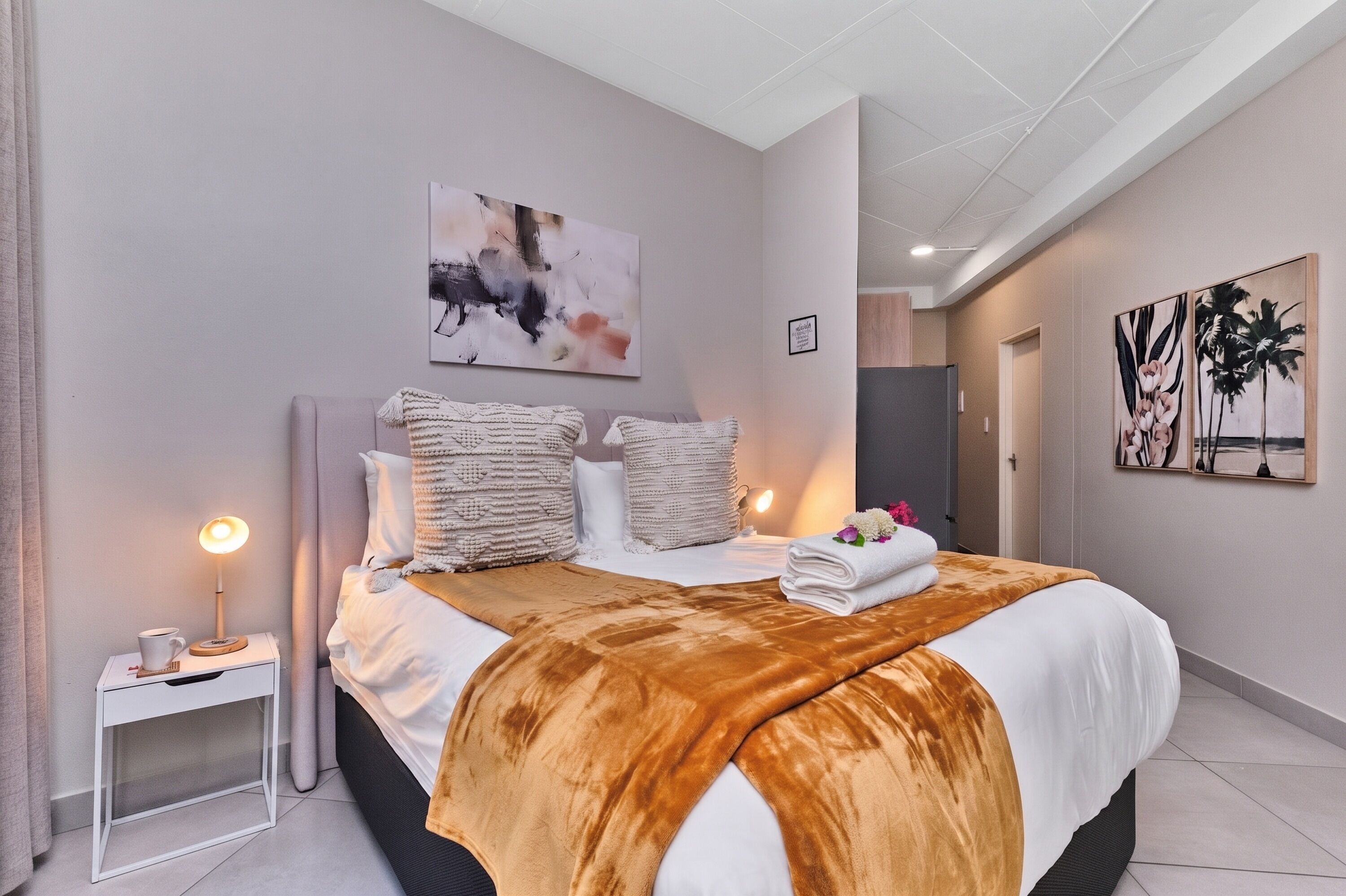 Une chambre d’hôtel avec un lit, des tables de chevet, une commode, un tableau et une porte donnant sur une autre pièce.