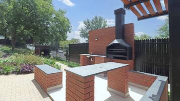 Area barbecue esterna con forno a mattoni, un tavolo e una struttura a pergola.