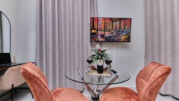 A modern living room with a glass table, two orange chairs, a painting on the wall, and a fireplace.