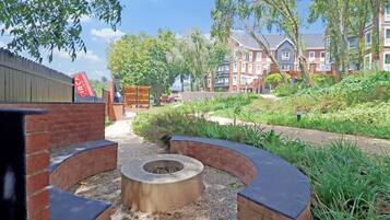 A courtyard with a circular seating area, a brick wall, and a pathway leading to a building with multiple windows.