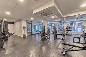 Een sportschool met diverse fitnessapparaten, grote ramen en een plant.