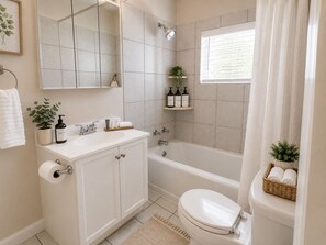 Ein Badezimmer mit weißem Waschbecken, Spiegel und Toilette, einem Duschbereich und einem Fenster mit Jalousien.