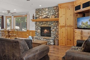 A cozy living room with a stone fireplace, wooden furniture, and a television. - Après-Ski Romantic Retreat | Hot Tub | AC | Dogs (Big Bear Lake)