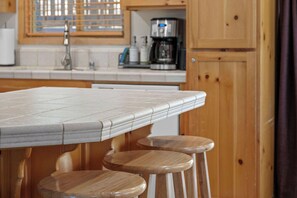 Una cucina con un piano di lavoro piastrellato, sgabelli di legno e una macchina da caffè.