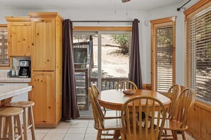 A kitchen with wooden cabinets, a dining table with chairs, and a view through a glass door to an outdoor area. - Après-Ski Romantic Retreat | Hot Tub | AC | Dogs (Big Bear Lake)