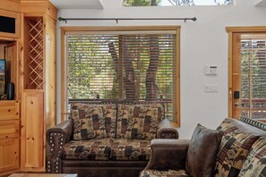 A cozy living room with a wooden bench, patterned cushions, and a large window with blinds. - Après-Ski Romantic Retreat | Hot Tub | AC | Dogs (Big Bear Lake)