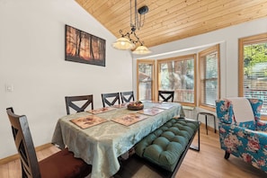 A dining area with a table set for four, a bench, and a floral armchair. - Big Bear House | Hot Tub | Summit Shuttle | Max 11 (Big Bear Lake)