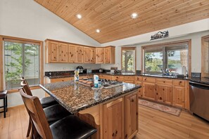 A modern kitchen with wooden cabinets, granite countertops, and a central island with seating. - Big Bear House | Hot Tub | Summit Shuttle | Max 11 (Big Bear Lake)