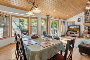 A dining area with a table set for four, surrounded by chairs, and a television in the background. - Big Bear House | Hot Tub | Summit Shuttle | Max 11 (Big Bear Lake)