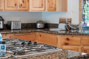 Una cocina con estufa a gas, encimera de granito, armarios de madera y una ventana con vistas.