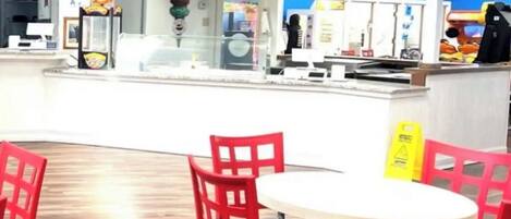 Una zona de comidas con una pizzería, un menú digital y sillas rojas alrededor de una mesa.