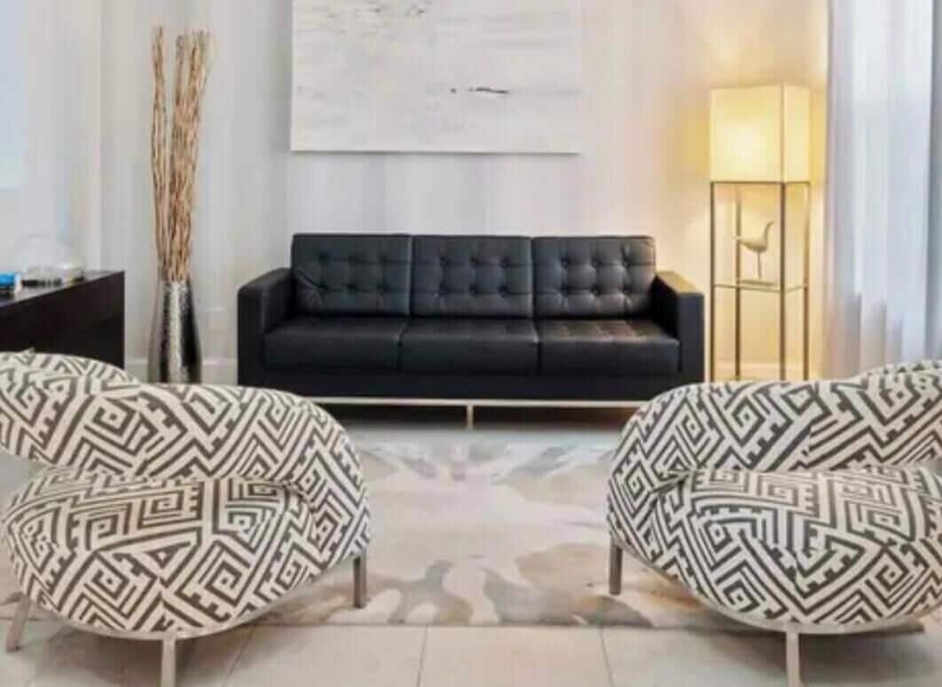 A living room with a black sofa, two patterned armchairs, a floor lamp, and a vase with tall, thin branches.