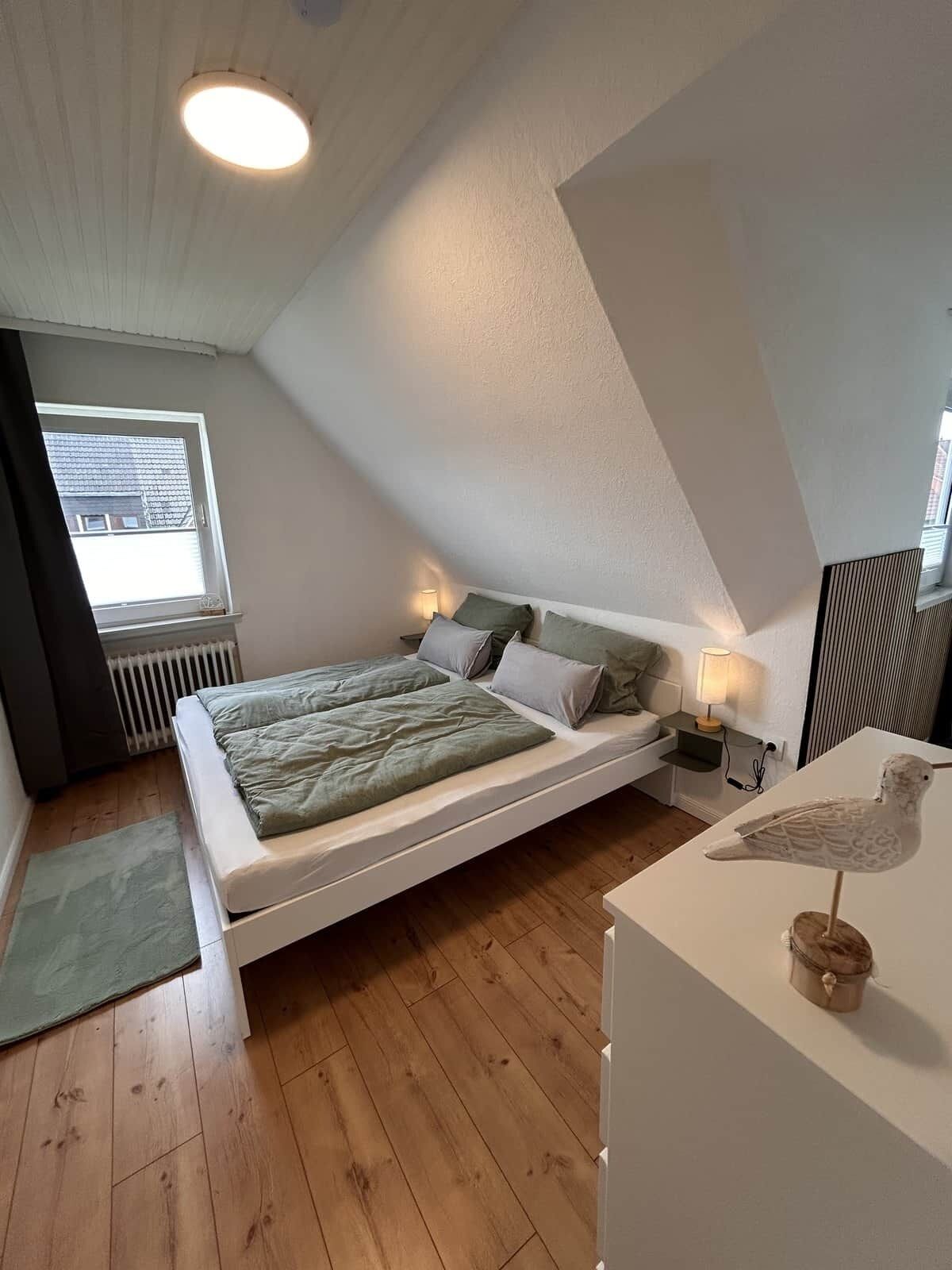 A bedroom with a sloped ceiling, a bed with pillows, a nightstand with a lamp, and a bird sculpture on a table.
