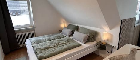 A bedroom with a sloped ceiling, a bed with pillows, a nightstand with a lamp, and a bird sculpture on a table.