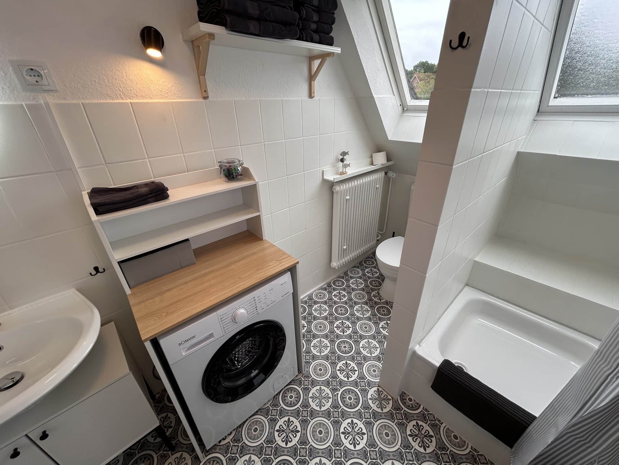 A compact bathroom with a washing machine, a radiator, and a window.