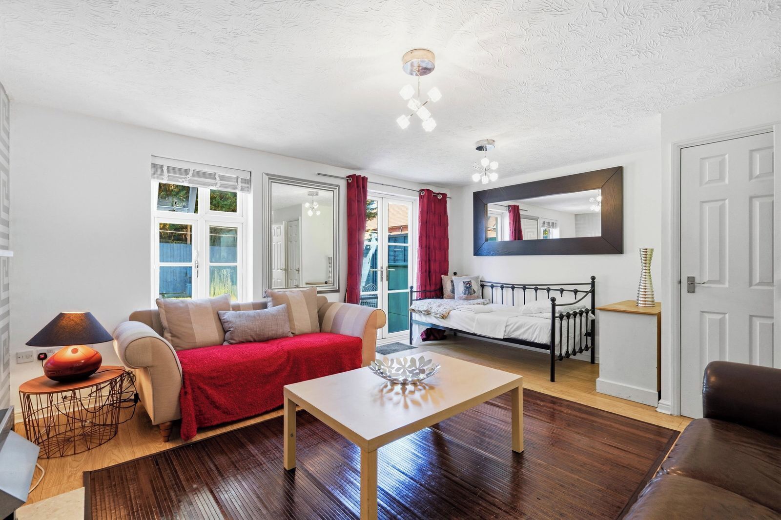 A room with a bed, a sofa, a table, and a mirror.