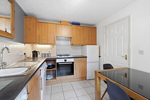 A compact kitchen with wooden cabinets, a gas stove, a built-in oven, and a refrigerator. - Modern 3BR Retreat|Garden & Parking (Solihull)