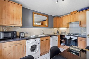 A compact kitchen with wooden cabinets, a microwave, a toaster, a sink, a washing machine, and a stove. - Modern 3BR Retreat|Garden & Parking (Solihull)