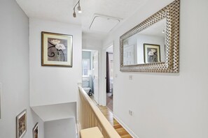 A hallway with a staircase, a framed picture, and a large mirror with a woven frame. - Modern 3BR Retreat|Garden & Parking (Solihull)