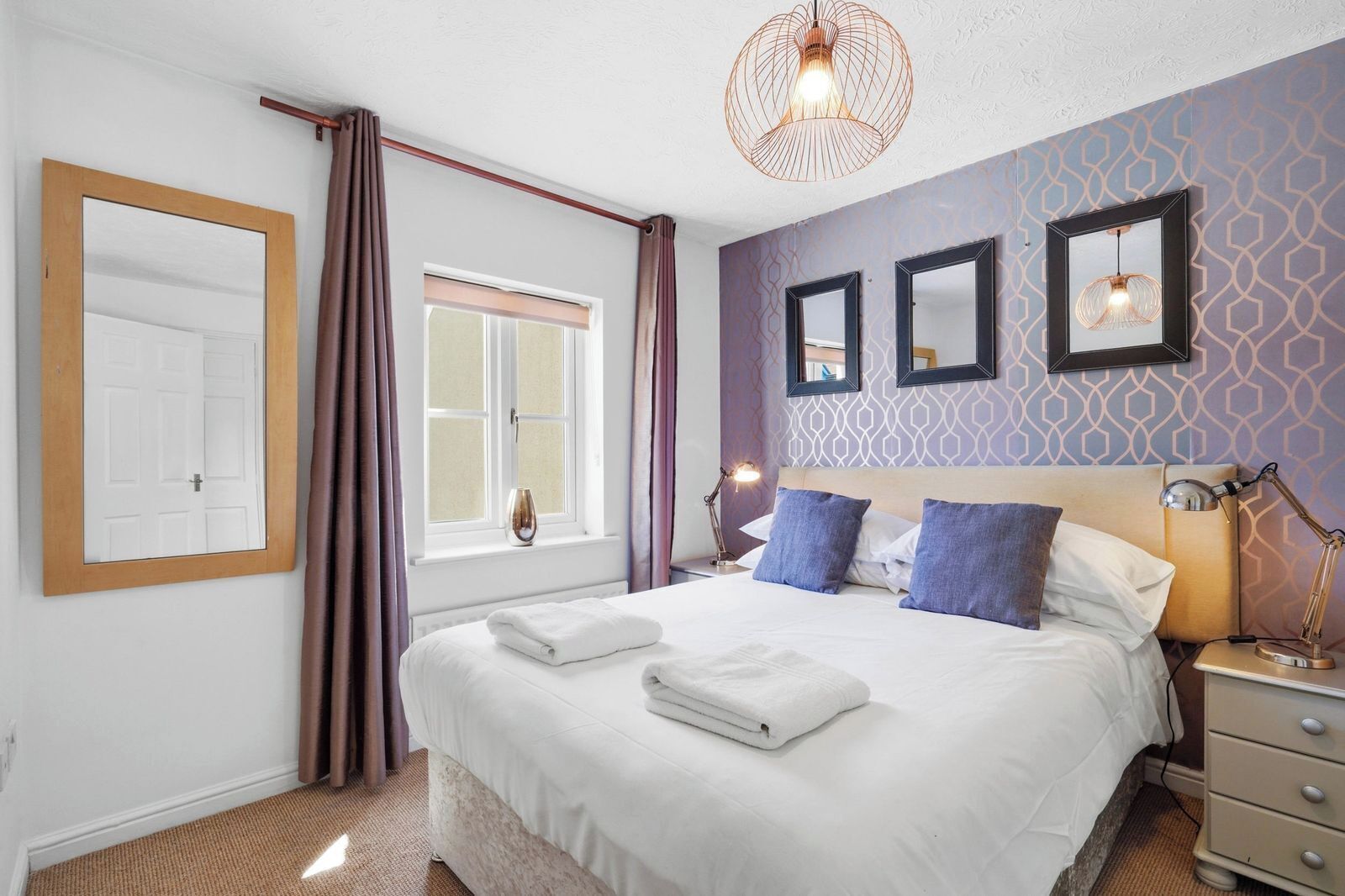 A neatly made bed with pillows, a bedside lamp, and a wall-mounted mirror.