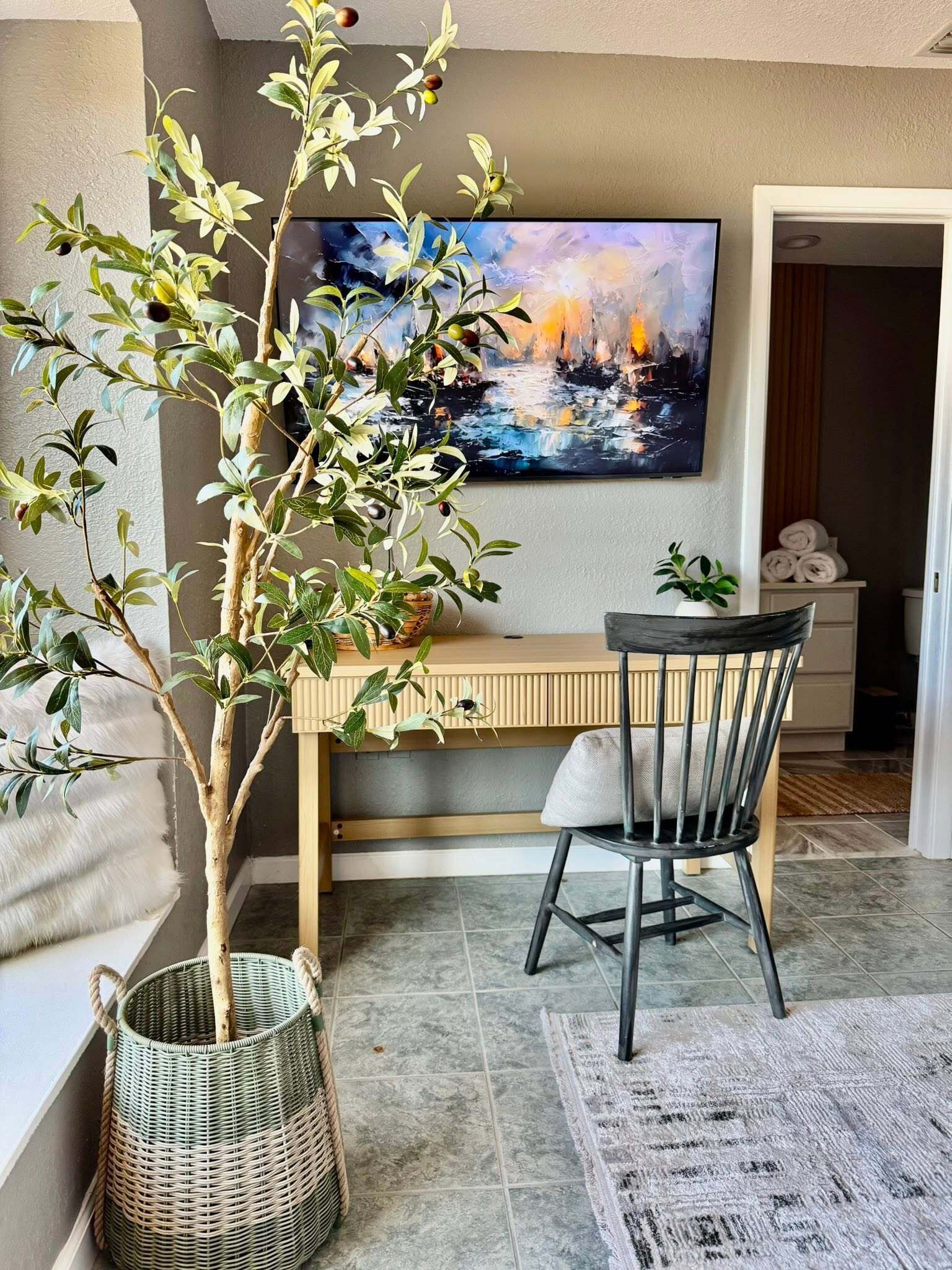 A room with a desk, chair, and a large painting on the wall.