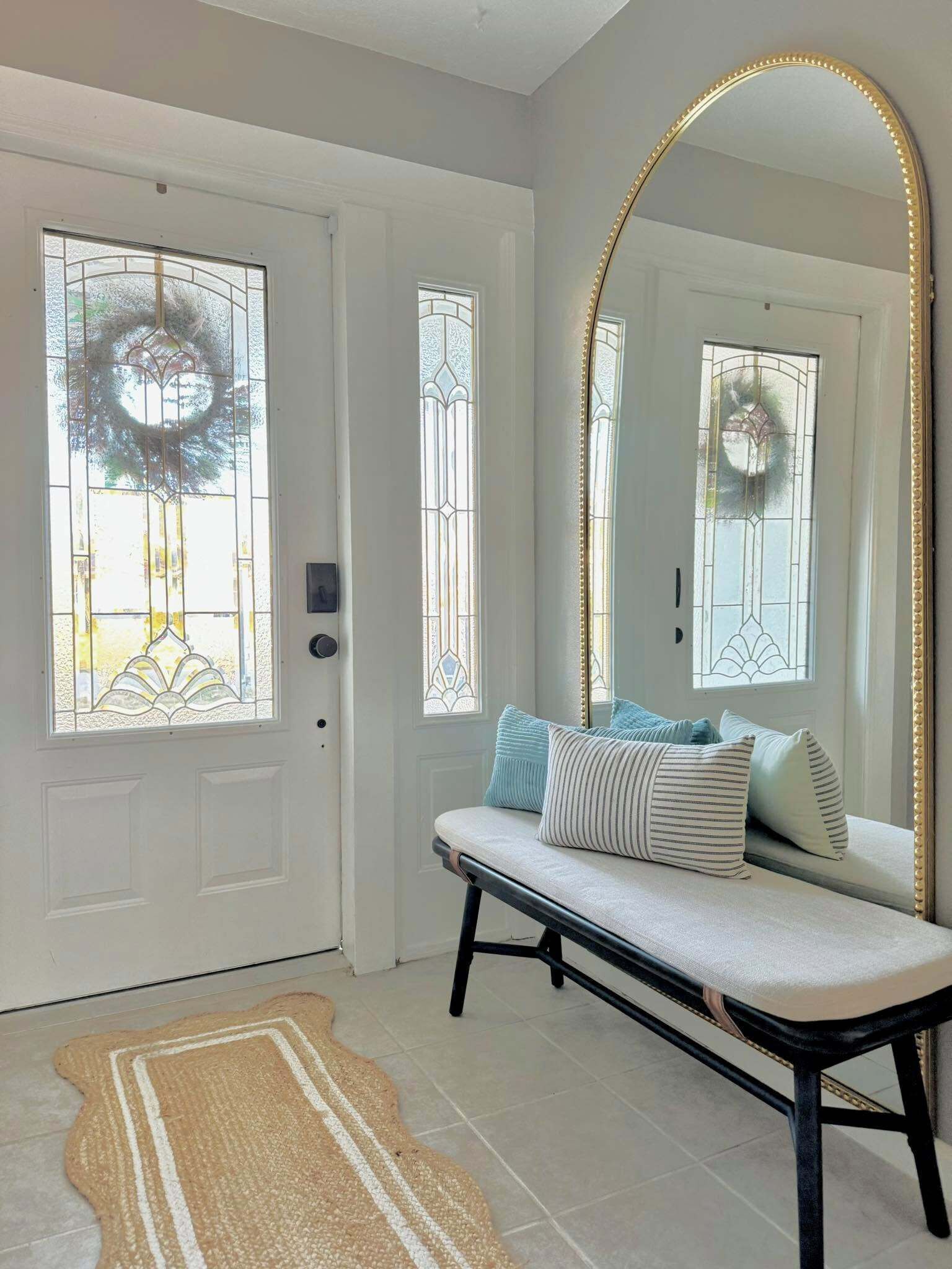 A room with a bench, a large mirror, and a rug.
