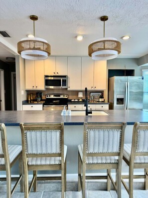A modern kitchen with a central island, stainless steel appliances, and a dining area with upholstered chairs. - 3 bed, 2 bath canal front house with boat lift and pool (Port Charlotte)