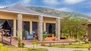 Un área de estar al aire libre con techo, pilares de piedra, una mesa y sillas, frente a un paisaje montañoso.