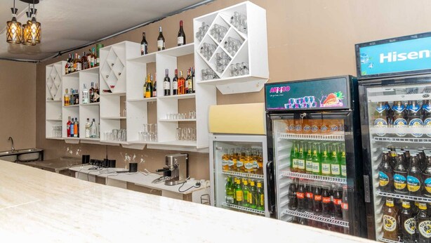 Zona de bar con estantes llenos de botellas de licor, una máquina de café y un refrigerador abastecido de bebidas.