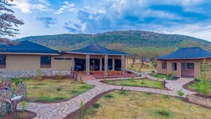 Un hotel con un área de estar cubierta al aire libre, senderos de piedra y montañas al fondo.