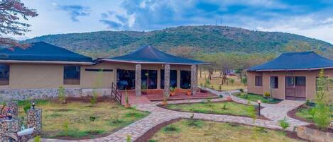Un hotel con un área de estar cubierta al aire libre, senderos de piedra y montañas al fondo.