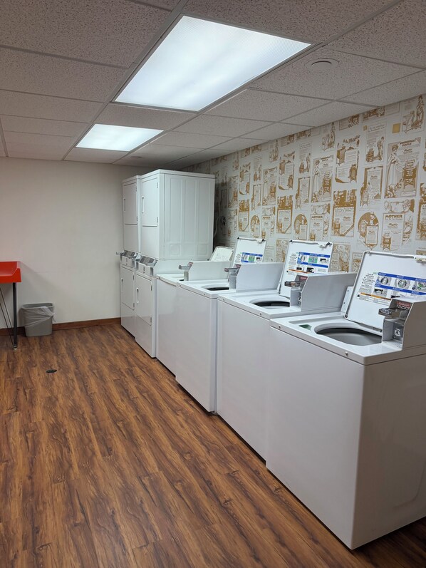 A laundry room with four front-loading washing machines, a white cabinet, and a red trash bin.