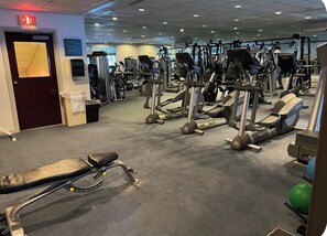 A gym with various exercise machines, a weight room sign, and a bench.