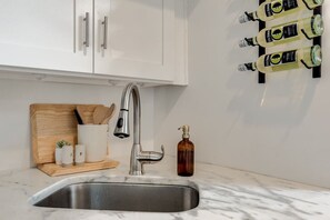 A kitchen with a stainless steel sink, white cabinets, a wooden cutting board with utensils, and a bottle of hand soap. - Gordon Studio — Bright and Airy 2nd Floor Carriage House in Savannah`s Historic District (Savannah)