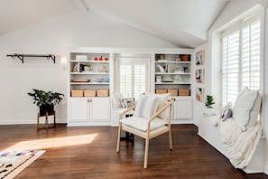 Ein Zimmer mit Holzboden, einem Sessel, einer weißen Bank und eingebauten Regalen mit Körben und Dekoration.