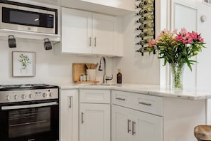 A modern kitchen with white cabinetry, a built-in microwave, a gas stove, and a wine rack. - Gordon Studio — Bright and Airy 2nd Floor Carriage House in Savannah`s Historic District (Savannah)