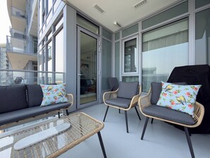 Ein Balkon mit Korbmöbeln, darunter eine Sitzecke mit Sofa und zwei Stühlen sowie ein Glastisch.