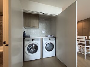 Ein kompakter Waschraum mit zwei Geräten für Frontlader, einer Arbeitsplatte mit Kaffeemaschine und einem Holzschrank darüber.