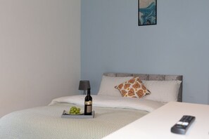 A hotel room with a bed, a bedside table with a bottle and grapes, a remote control, and a painting on the wall. - Studio Flat near University of Aberdeen (Aberdeen)