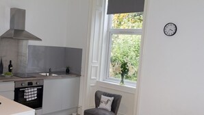 Eine kompakte Küche mit Herd, Backofen und Spüle, ein Fenster mit Blick auf Grünflächen und ein Stuhl mit Kissen.