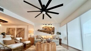 Un soggiorno moderno con una ventola a soffitto, una grande finestra e un rustico tavolino in legno.