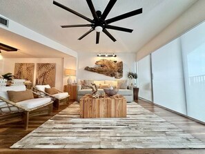 A modern living room with a ceiling fan, a large window, and a rustic wooden coffee table.