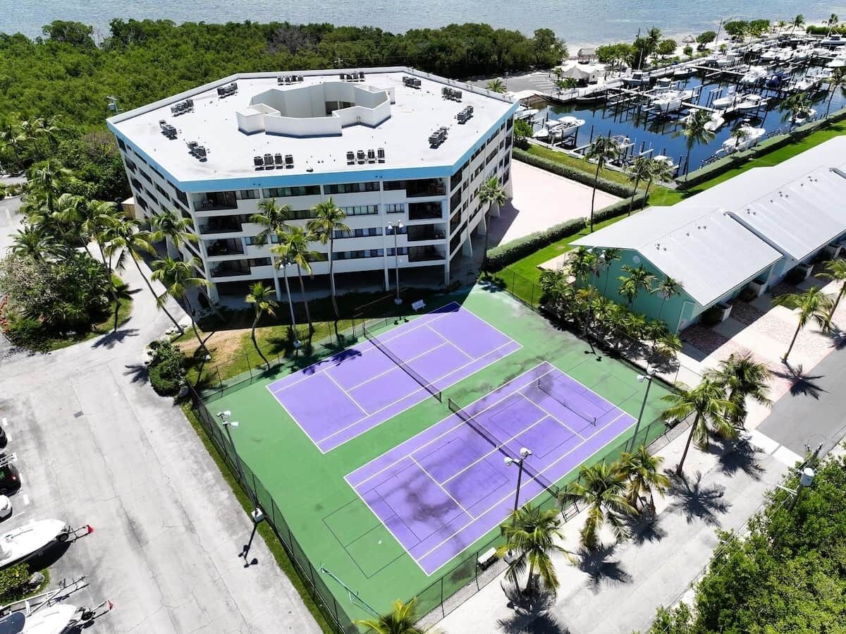 A multi-story building with a rooftop parking area, adjacent tennis courts, and a marina with boats.