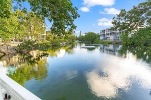 Une rivière paisible avec un quai, bordée d’arbres et surplombée d’un bâtiment au design moderne.