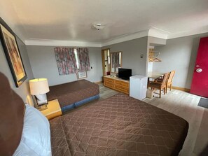 A hotel room with a bed, a desk with a computer, a chair, a wardrobe, and a red door.